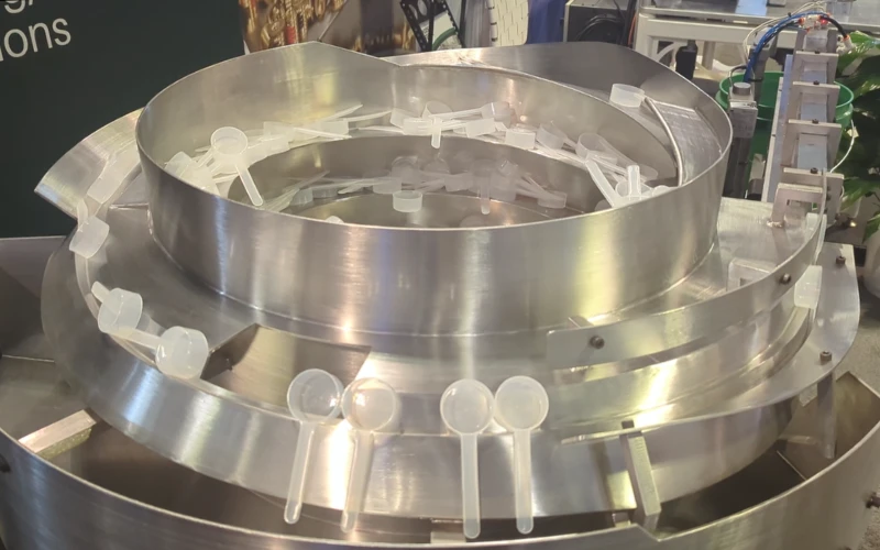 Overhead view of vibratory plastic scoop feeder system orienting plastic scoops for Pack Expo International